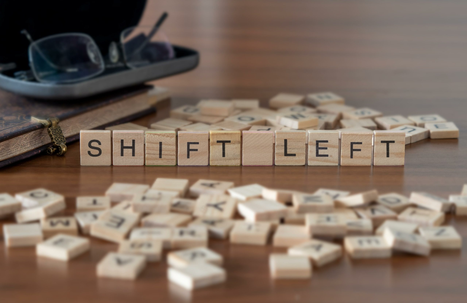 Wooden letter tiles spell "SHIFT LEFT" on a table, surrounded by scattered tiles and a pair of glasses on a notebook
